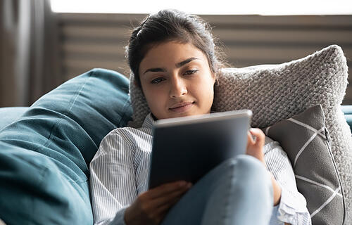 Young indian woman rest on sofa watching movie on tablet